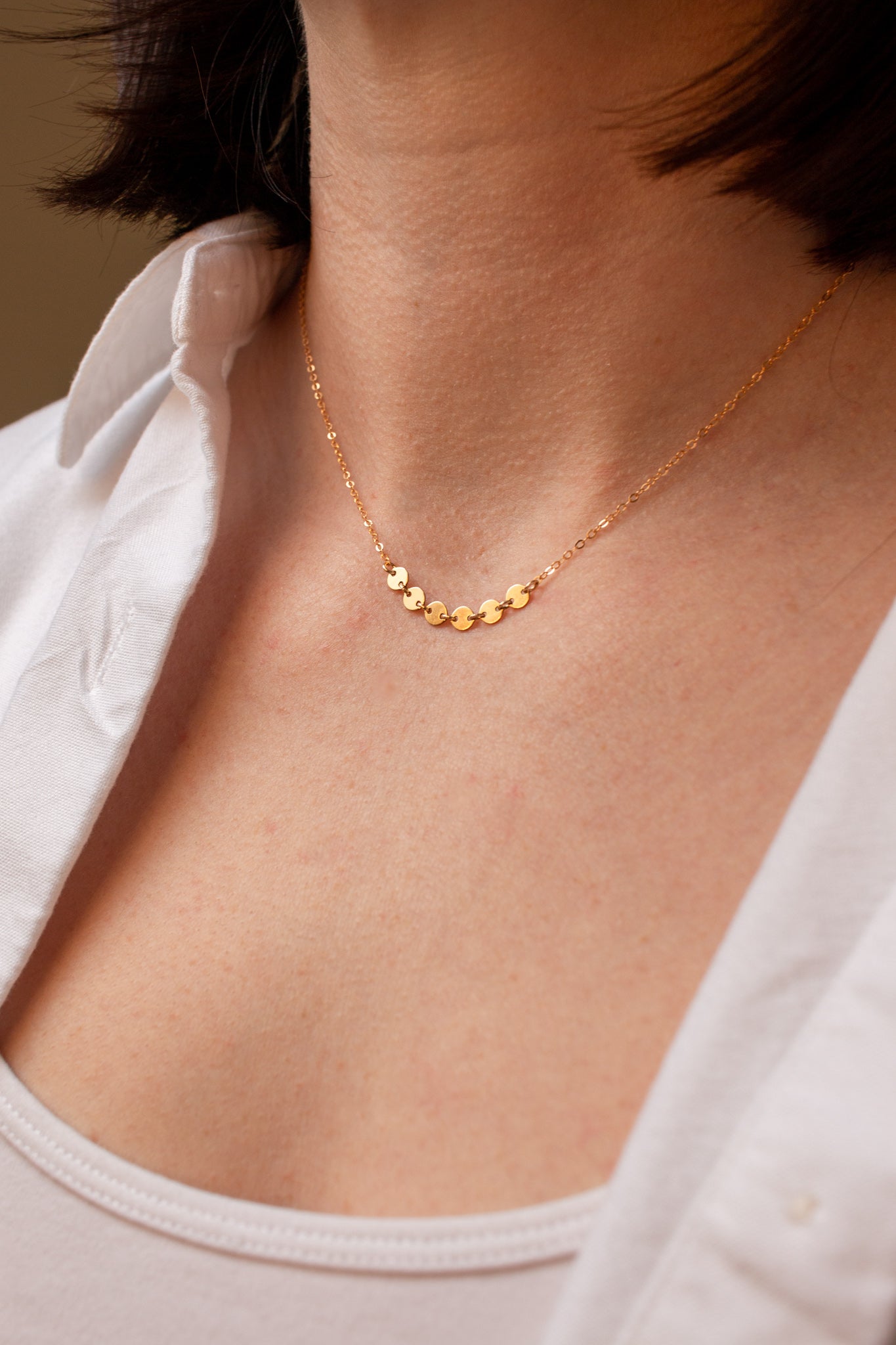 Gold necklace on a person wearing a white top against a neutral background