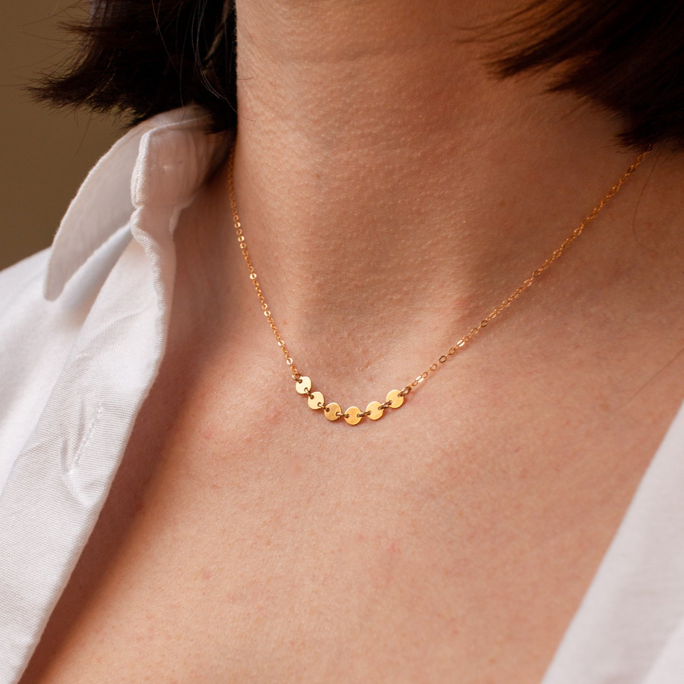 Gold necklace on a person wearing a white top against a neutral background