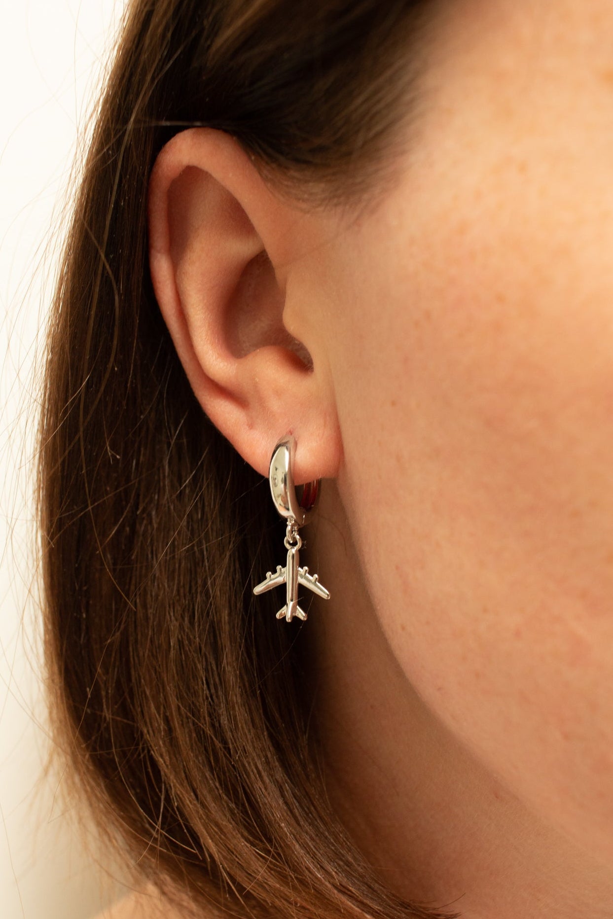 A close-up image of a person's ear wearing a gold-colored aviator-style earring with a jet charm.