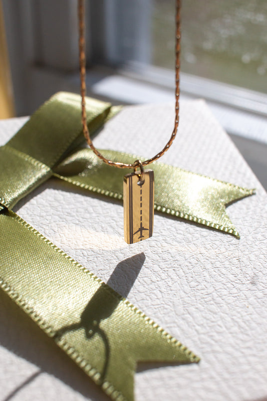 Gold rectangular necklace with a runway and airplane silhouette