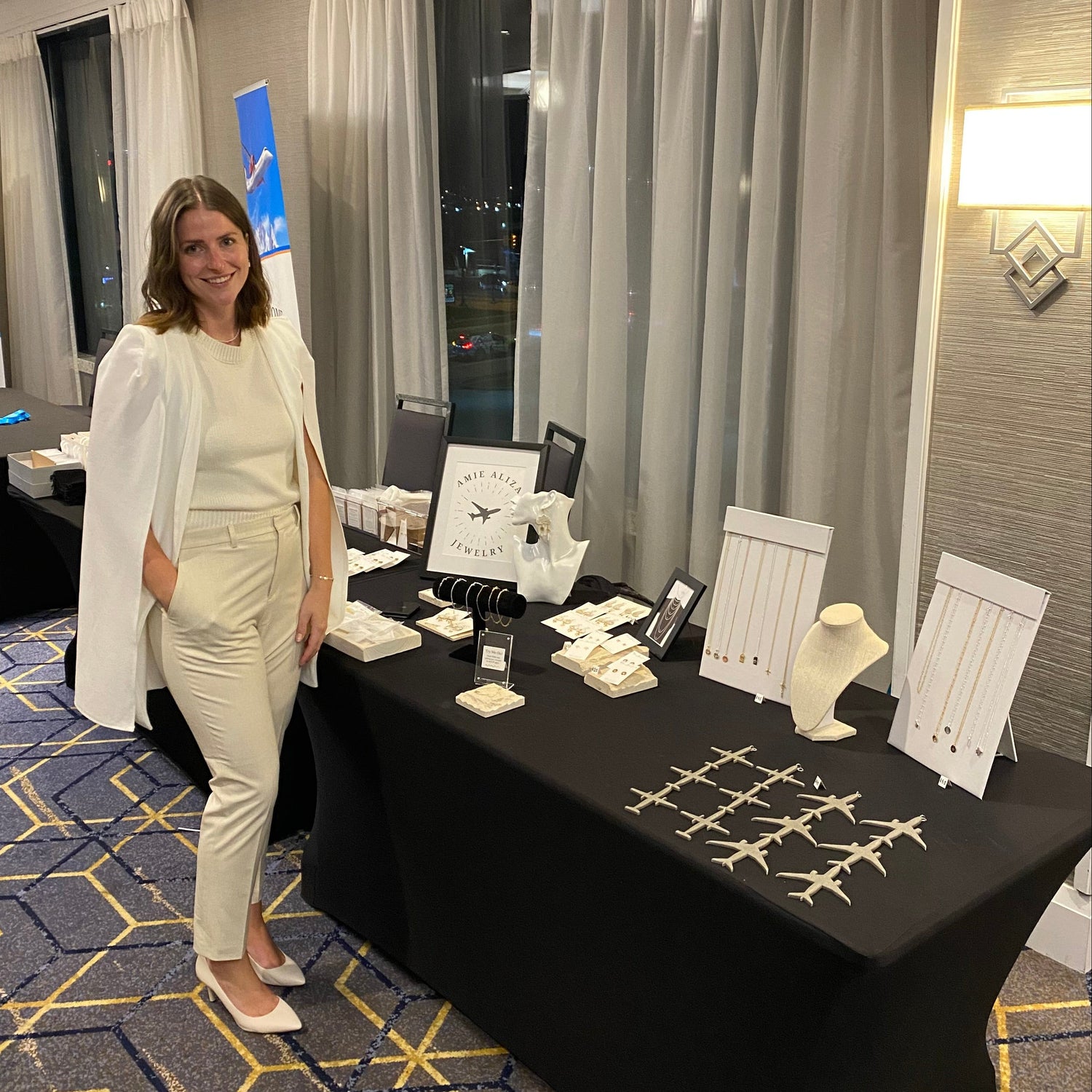 Owner and founder of Amie Aliza Jewelry, standing in front of her booth display at a women in aviation conference
